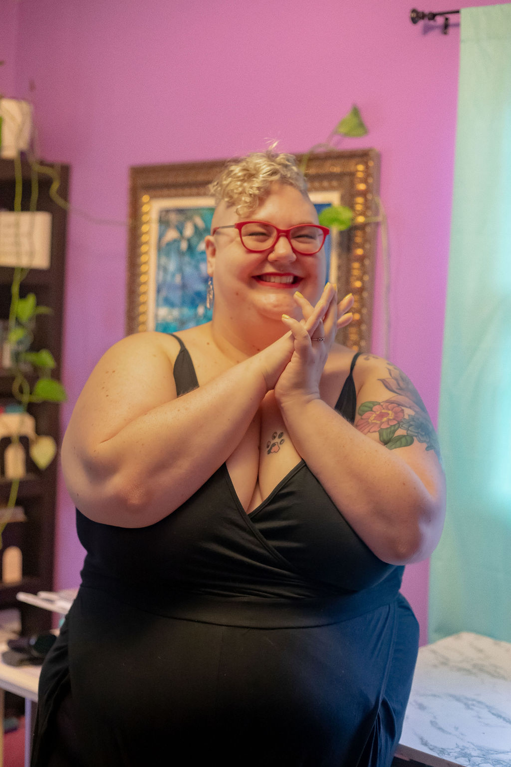 Caitlin is smiling so hard their face is all scrunched up, and their hands are clasped in front of their face in glee