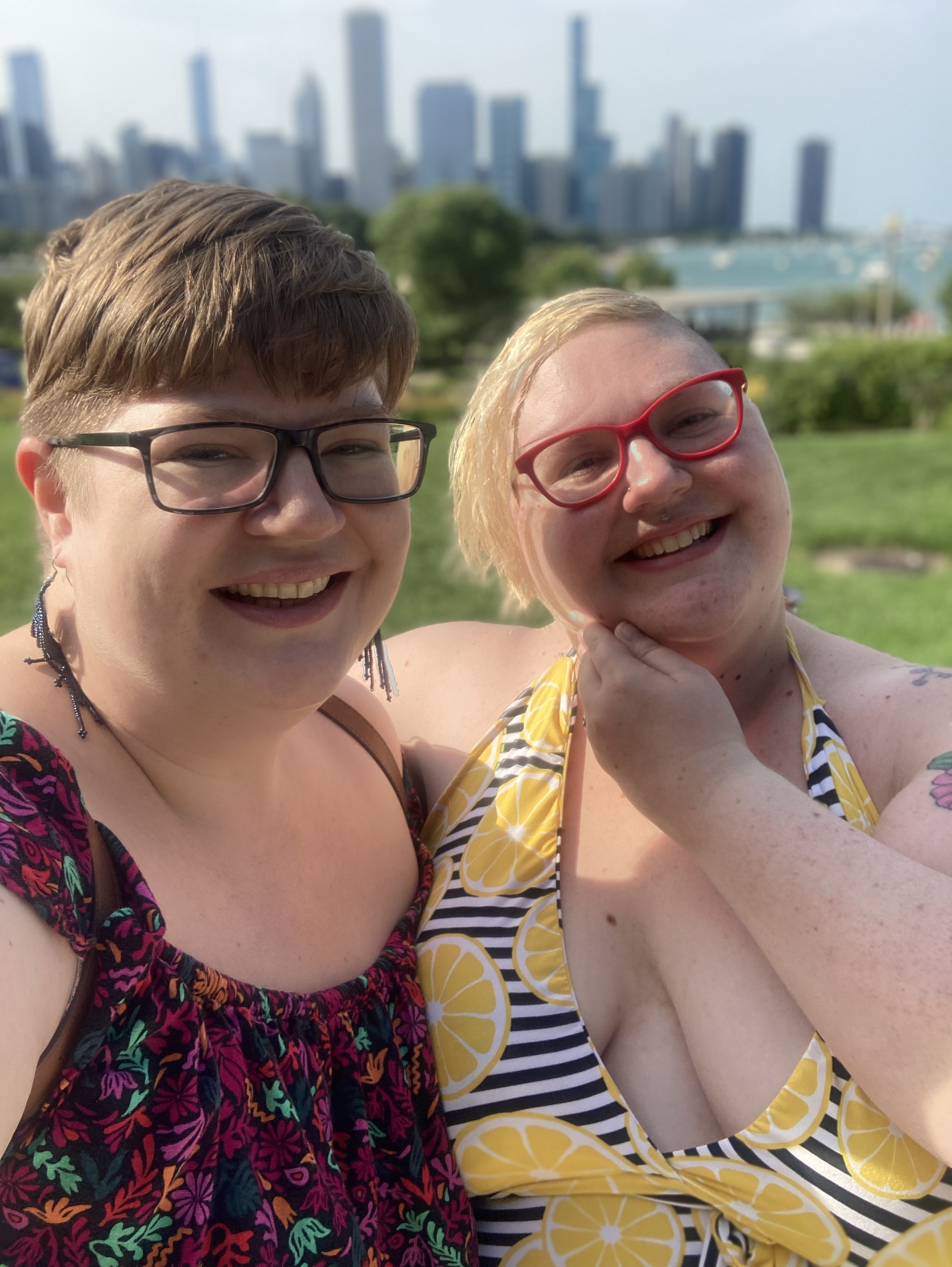 Caitlin smiling in a dress with black and white stripes and lemons, with their arm around their sibling Jess, also smiling at the camera.